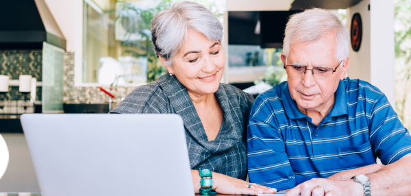Older man and woman smiling and looking down at calculator and paper