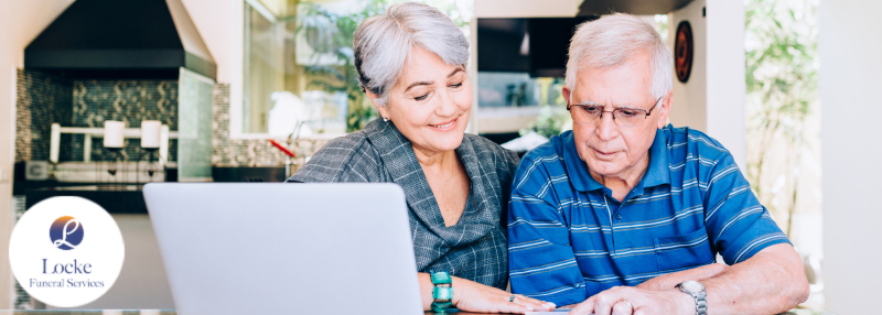 Older man and woman smiling and looking down at calculator and paper