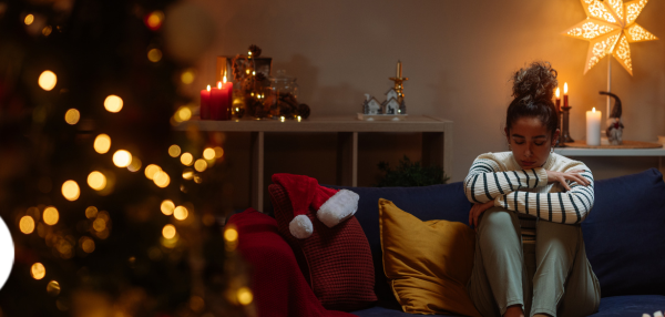 Woman sitting on couch alone with house decorated for holidays