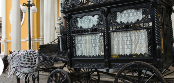 Horse-drawn black hearse in front of bright yellow building