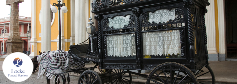 Horse-drawn black hearse in front of bright yellow building