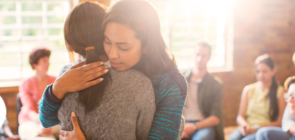 Two women hugging while support group of various people looks on