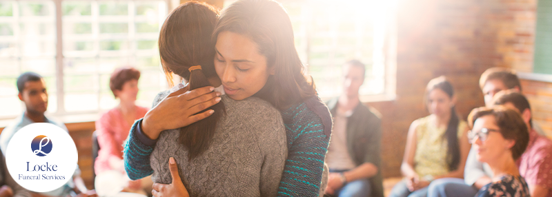 Two women hugging while support group of various people looks on