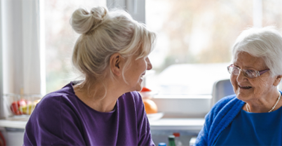 Image shows an older and younger woman talking in their home